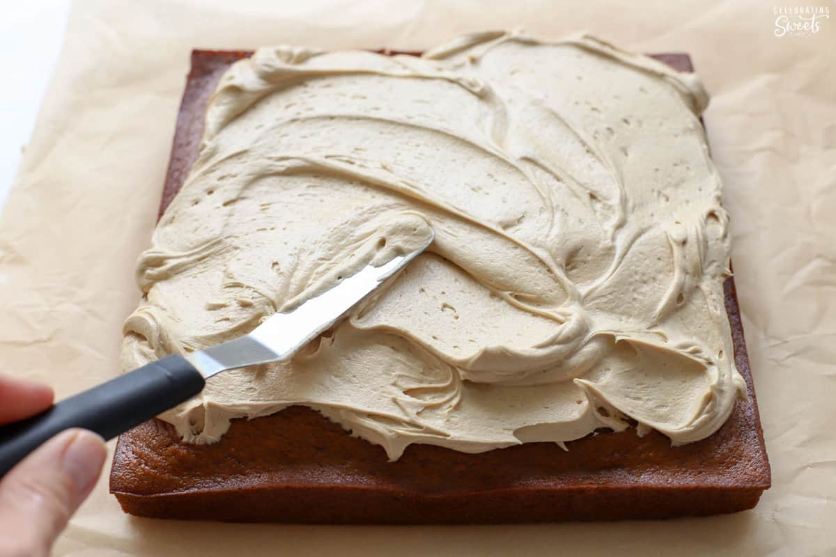 Frosting being spread on a square pumpkin cake.