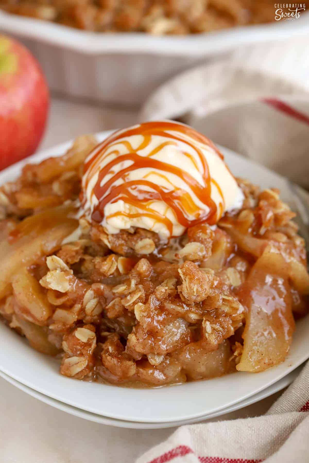 Apple crisp on a white plate topped with vanilla ice cream and caramel sauce.