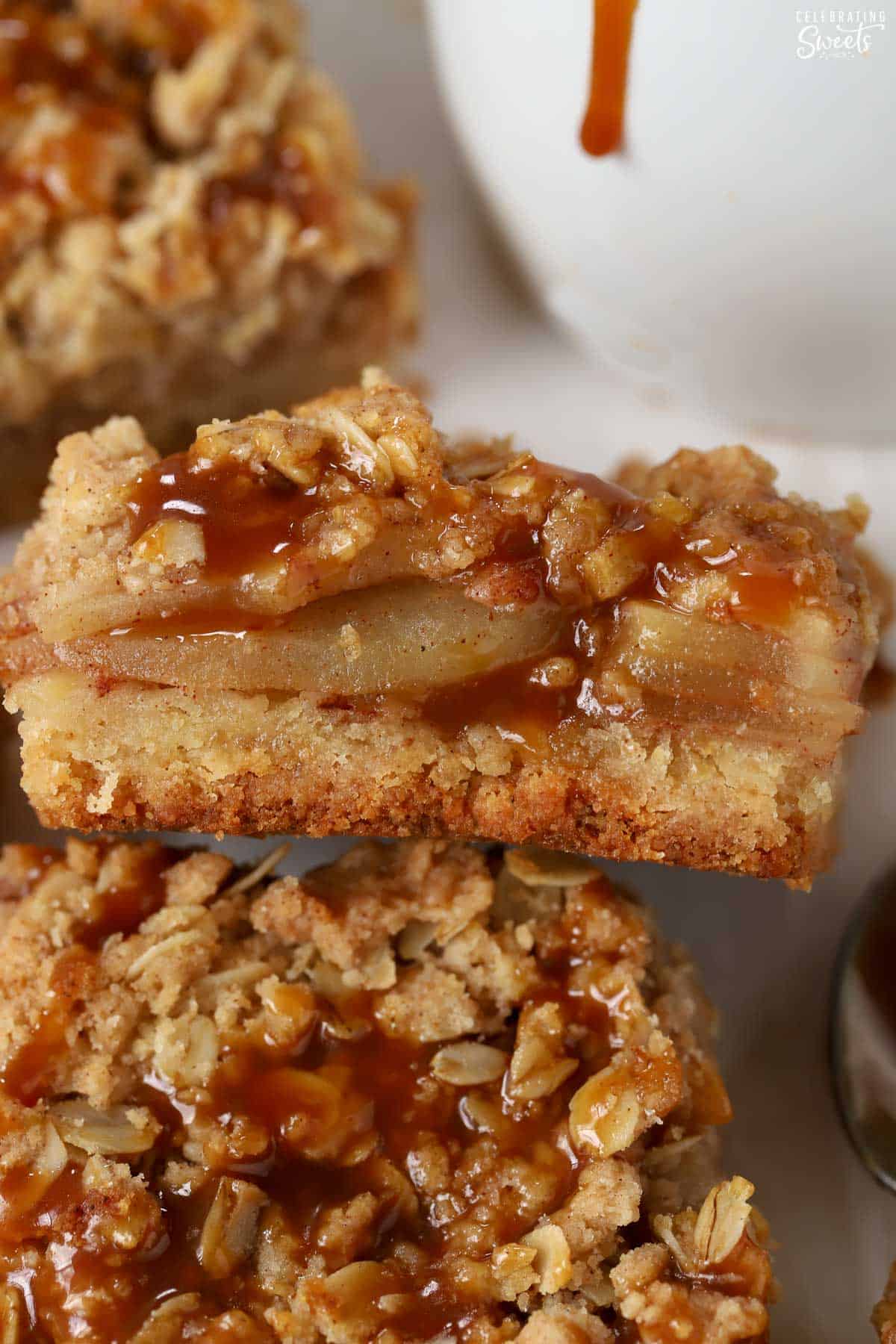 Close up of an apple crumb bar next to a white jar of caramel sauce.