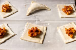 Unbaked apple turnovers on a parchment lined baking sheet.
