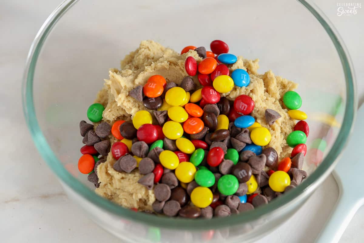 Cookie dough, M&M's, and chocolate chips in a glass bowl.