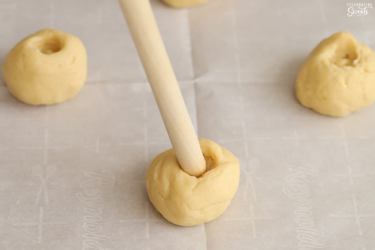 End of a wooden spoon being pushed into a ball of cookie dough.