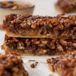 Stack of chocolate pecan bars on white parchment paper.