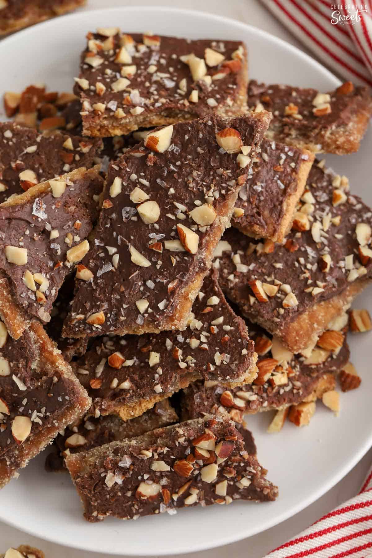 Graham cracker toffee topped with chopped almonds on a white plate next to a red and white striped napkin.