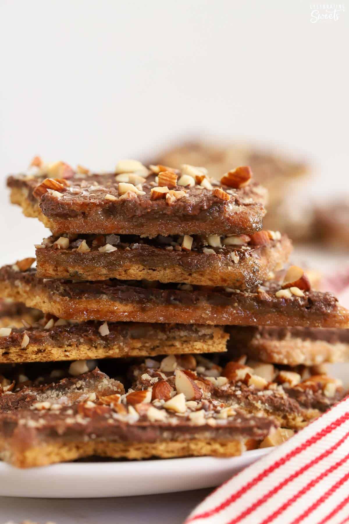 Stack of graham cracker toffee on a white plate next to a red and white striped napkin.