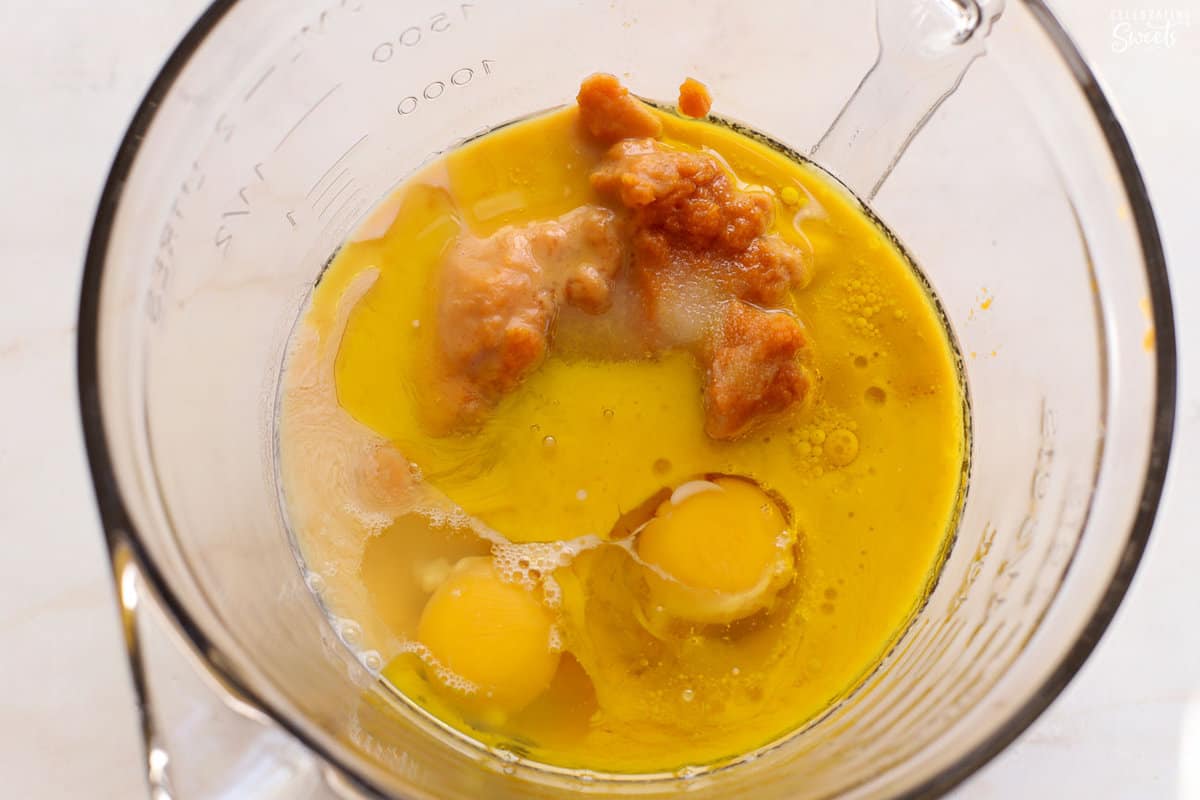 Glass bowl filled with pumpkin, sugar, eggs, and oil.