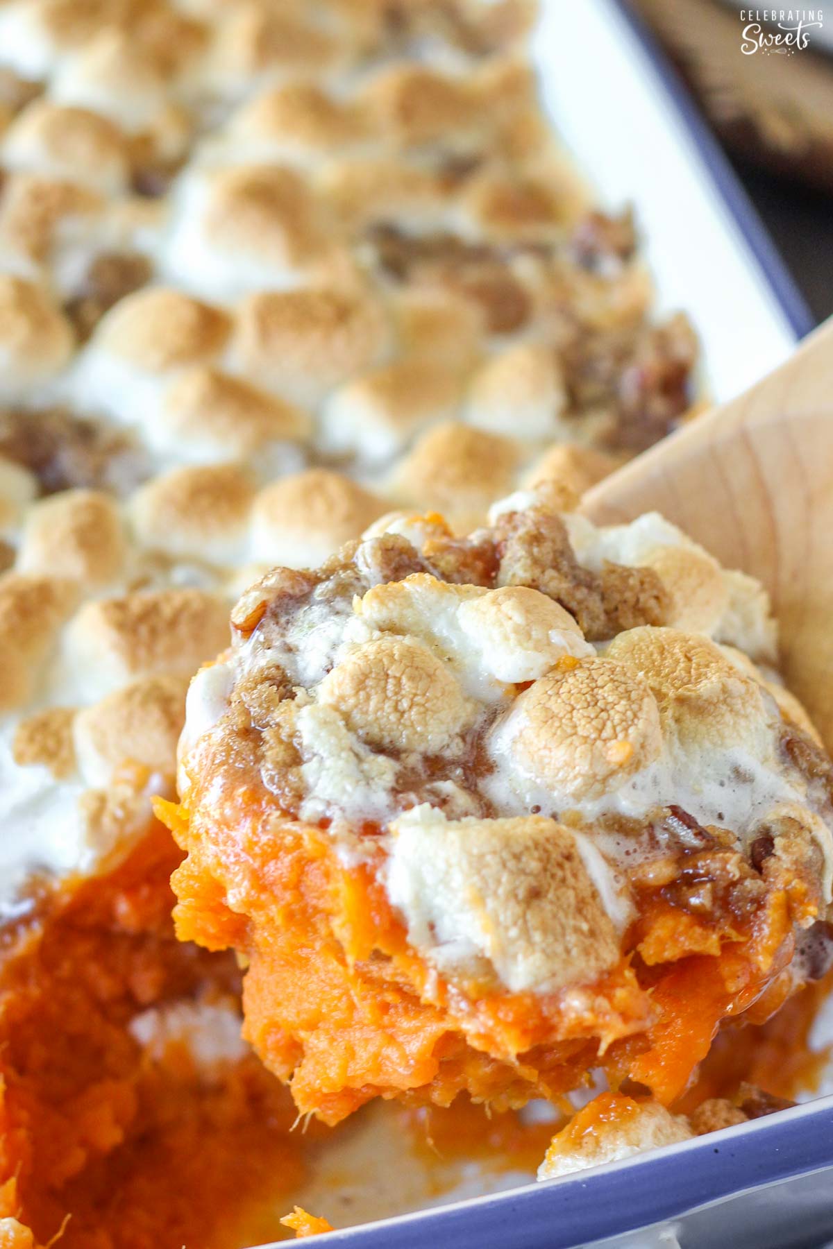 Scoop of sweet potato casserole with marshmallows on a wooden spoon.
