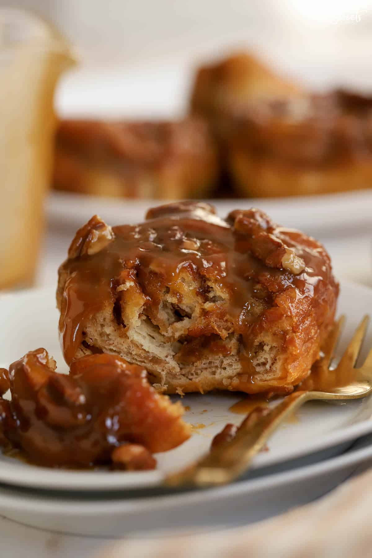 Sticky bun cut open on a white plate with a gold fork.