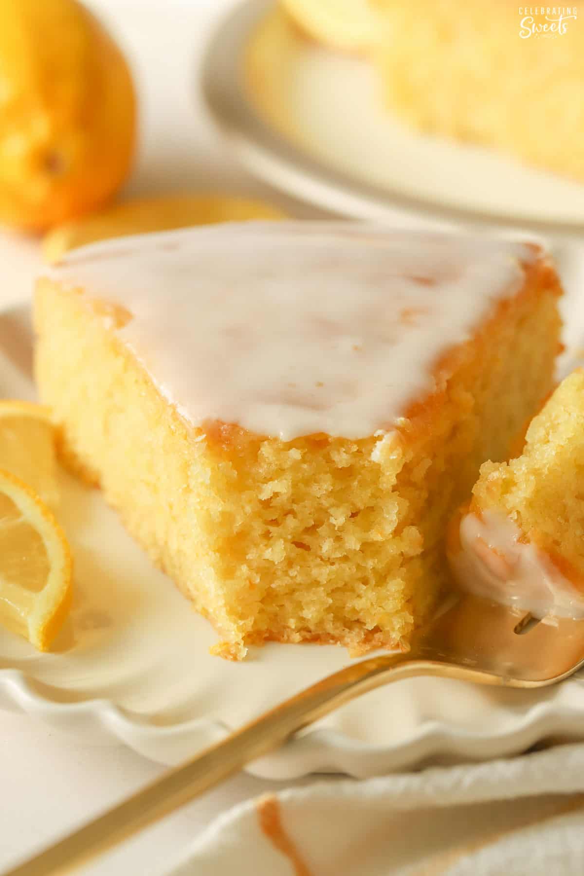 Slice of lemon olive oil cake on a white plate with a gold fork.