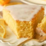 Slice of lemon olive oil cake on a white plate with a gold fork.