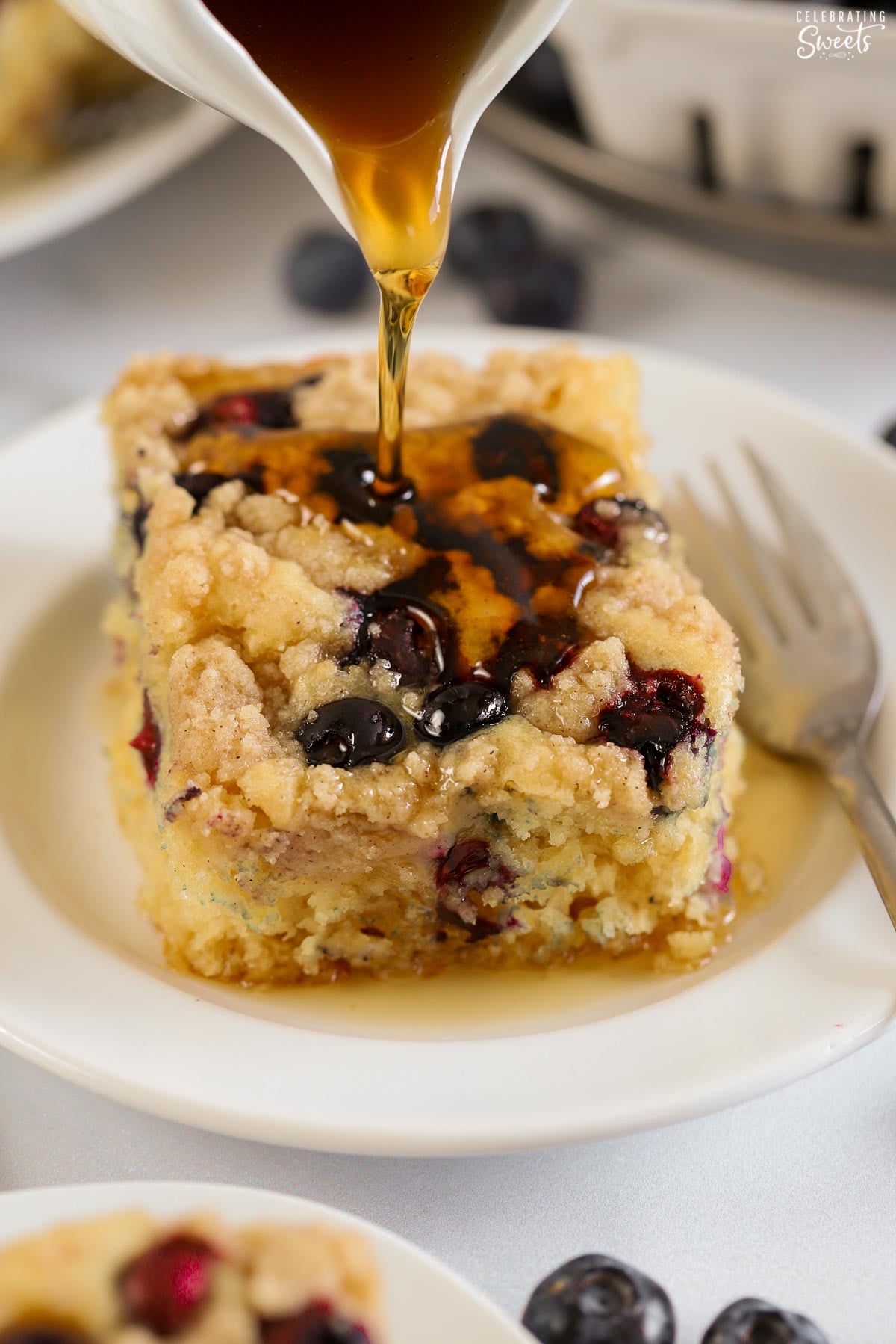 Syrup being poured on a slice of blueberry pancake casserole.