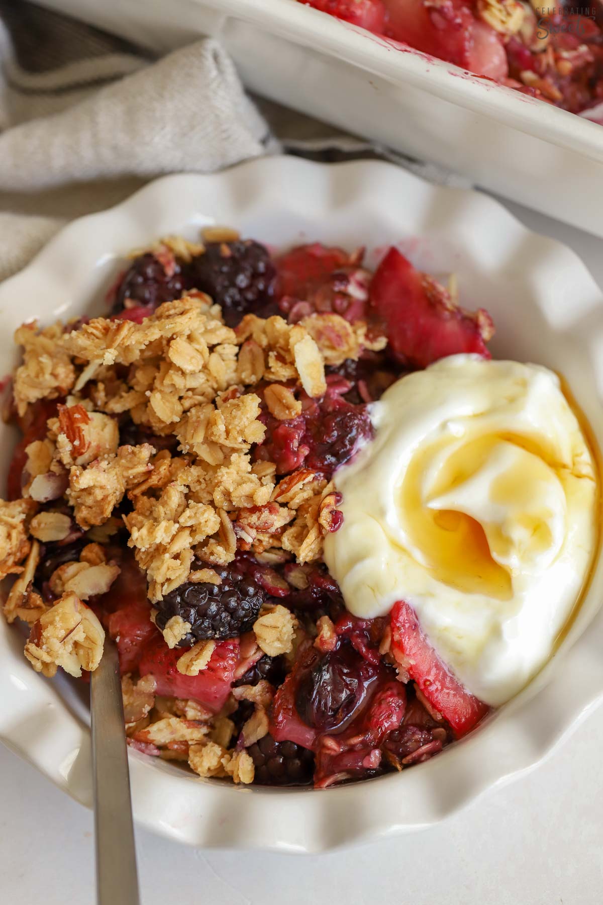 Closeup of a berry crisp with a scoop of yogurt in a white bowl.