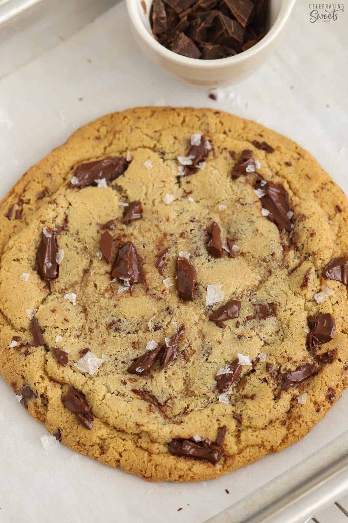 Closeup of a large chocolate chip cookie on a parchment lined baking sheet.