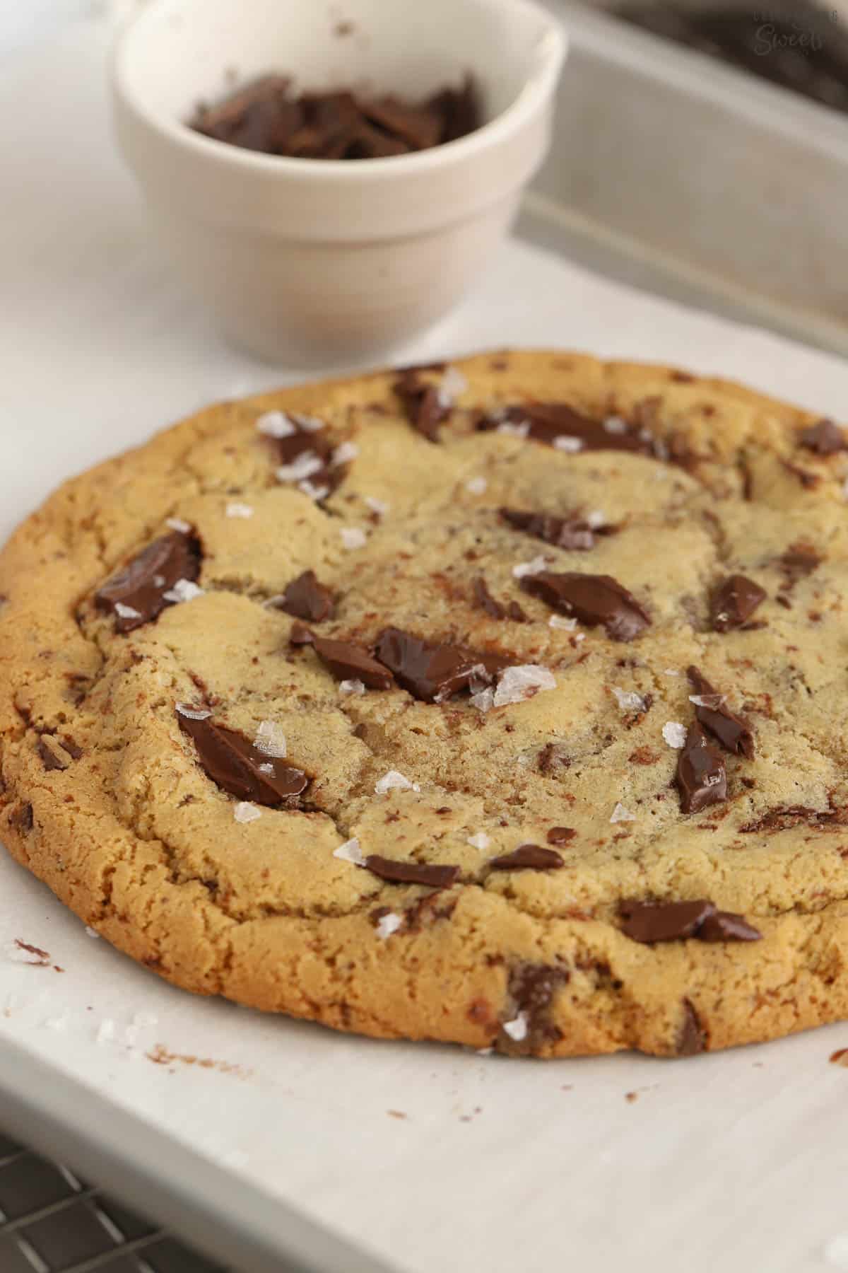 Closeup of a large chocolate chip cookie on a parchment lined baking sheet.