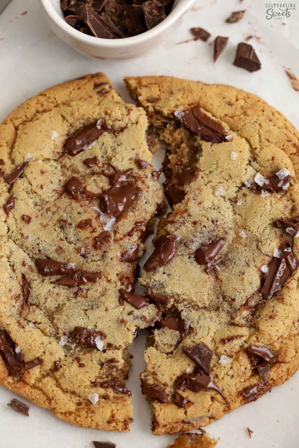Two pieces of a large chocolate chip on a parchment lined baking sheet.