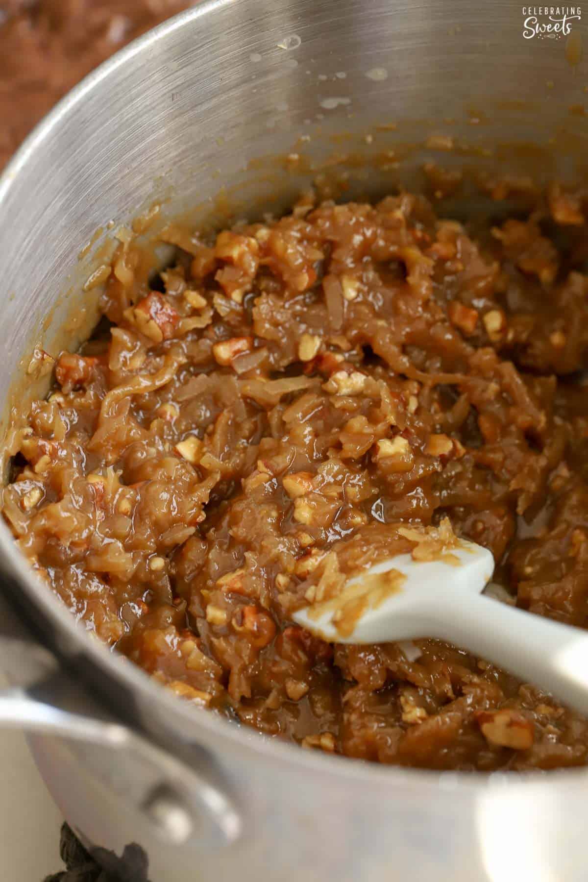 German chocolate (coconut pecan) frosting in a saucepan next to a grey spatula.