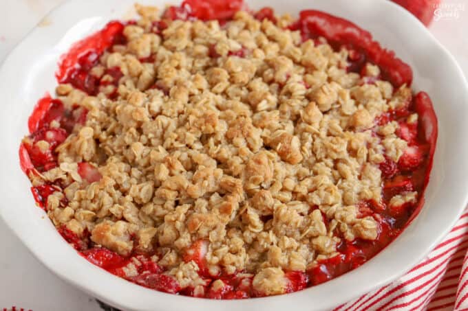 Strawberry crisp in a white baking dish next to a red and white striped towel.