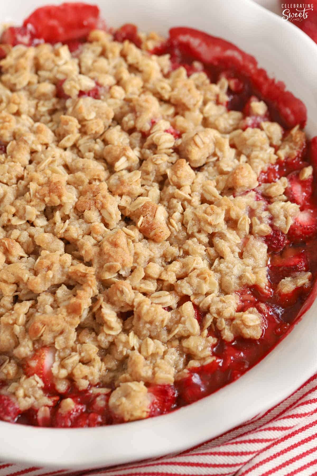 Strawberry crisp in a white baking dish next to a red and white striped towel.