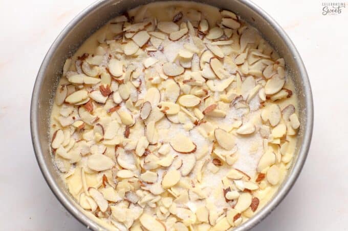 Cake batter in a round cake pan topped with sliced almonds and sugar.
