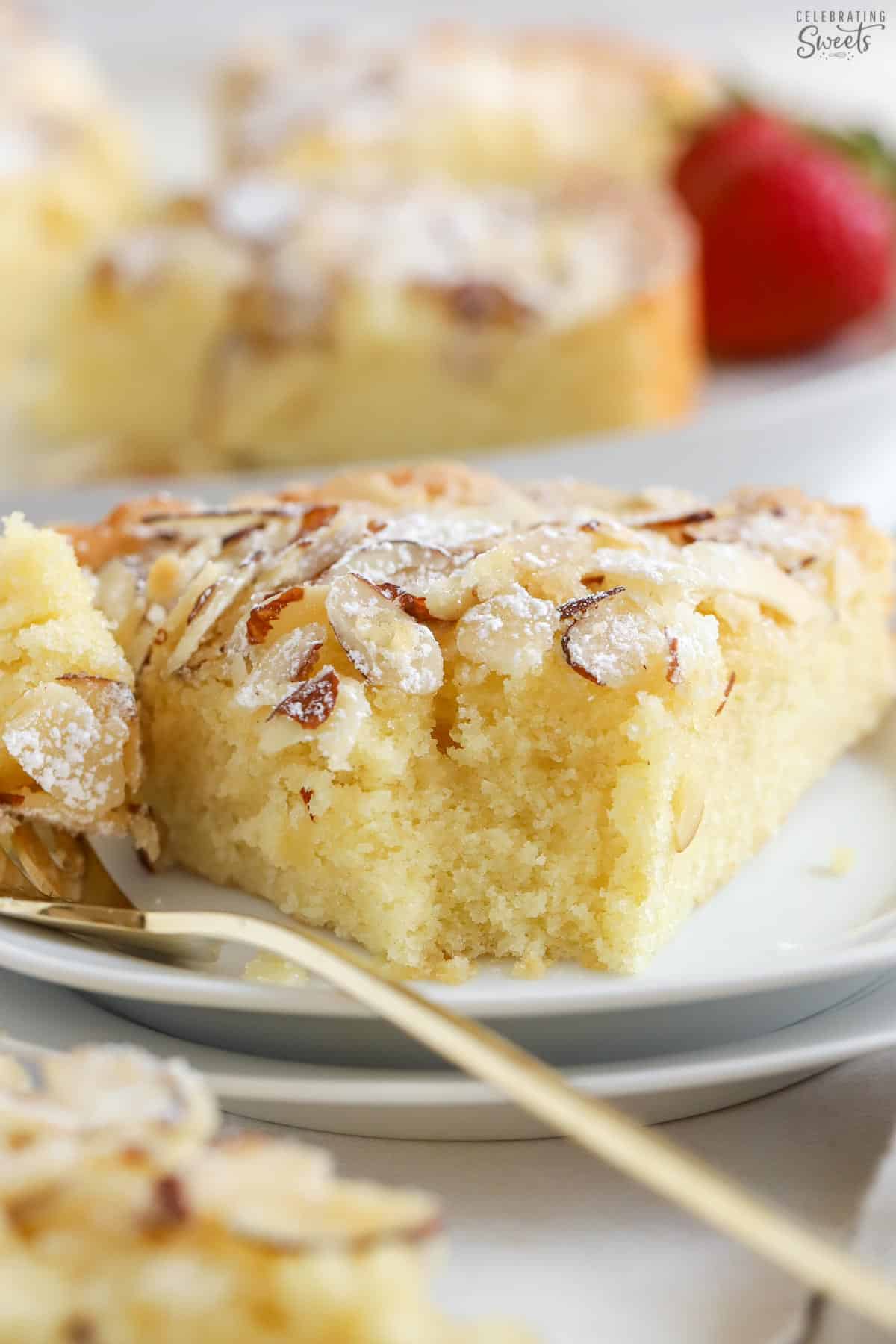 Slice of almond cake on a white plate with a gold fork.