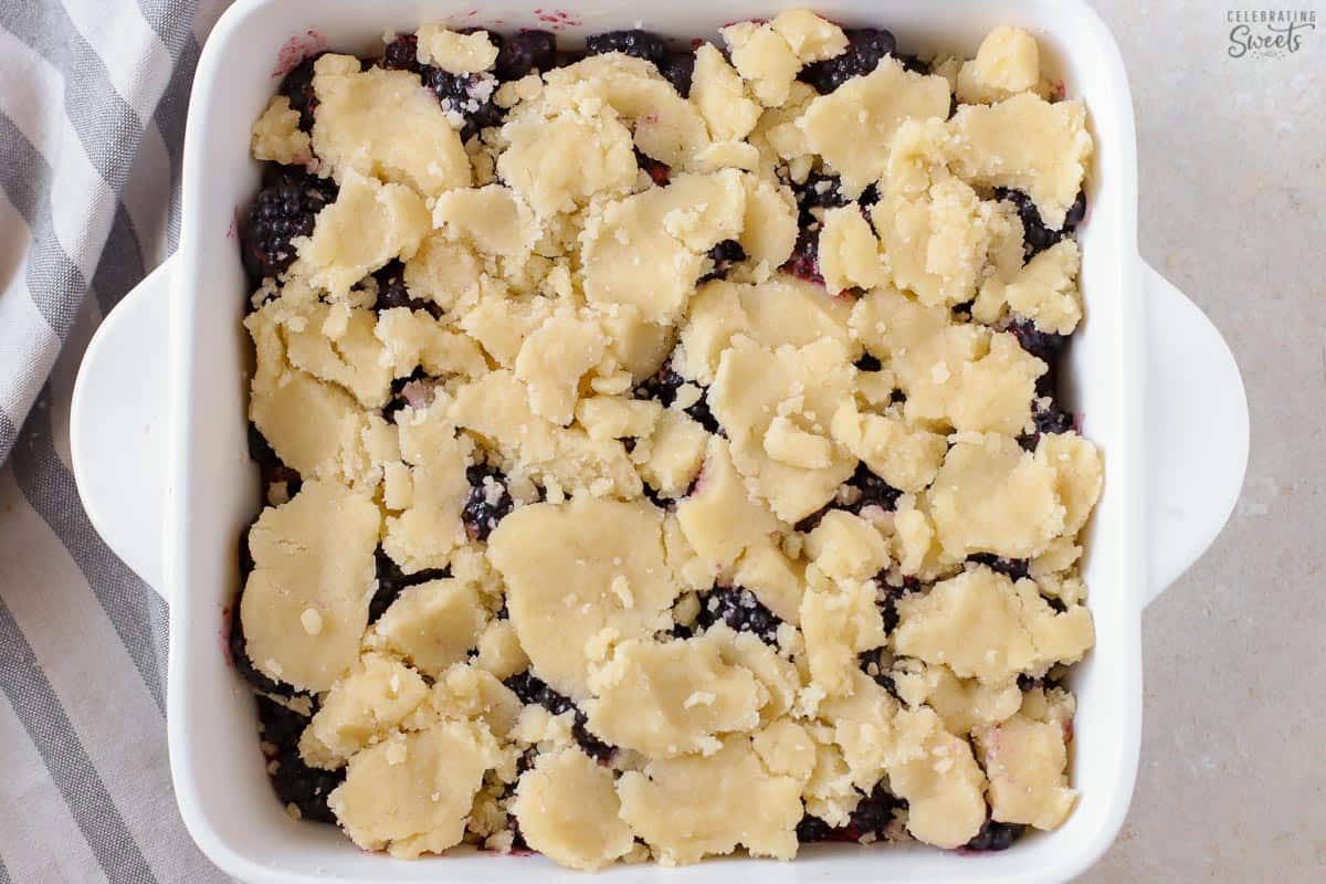 Unbaked blackberry cobbler in a white baking dish next to a white and blue towel.