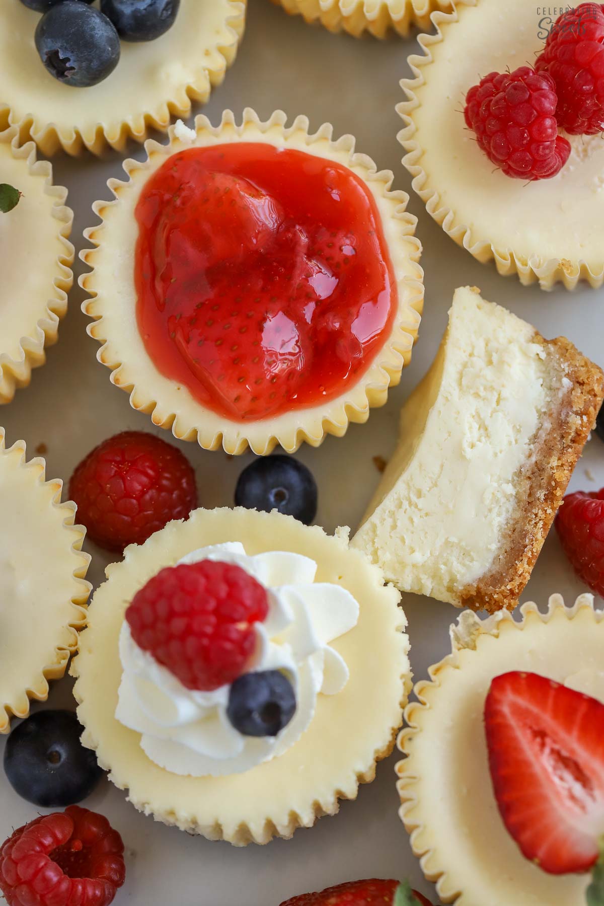 Mini cheesecakes on a grey plate topped with berries and whipped cream.