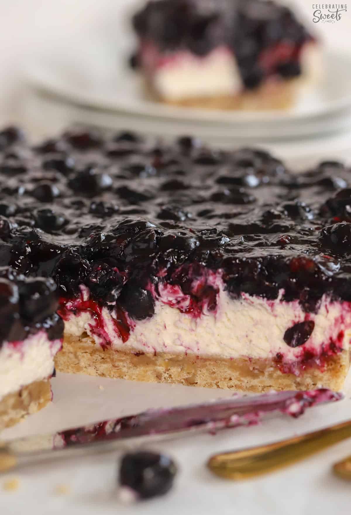Blueberry dessert bars on parchment paper next to a gold fork.