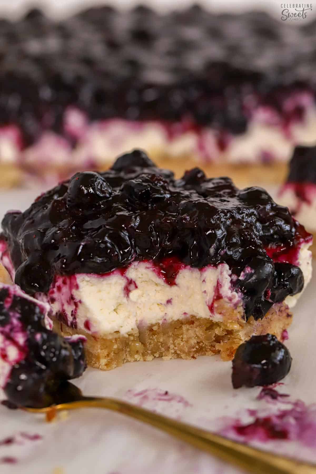 Blueberry dessert bar on parchment paper next to a gold fork.