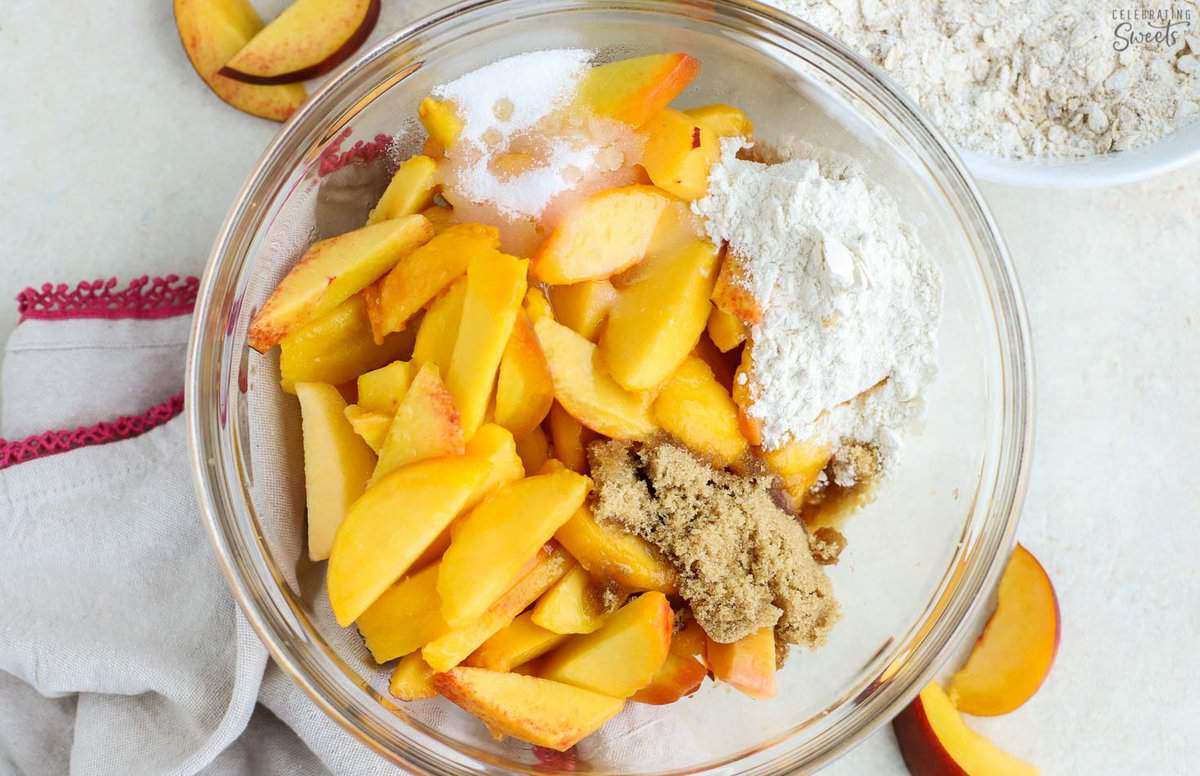 Filling for a peach crisp in a glass bowl (peaches, sugar, flour, cinnamon).