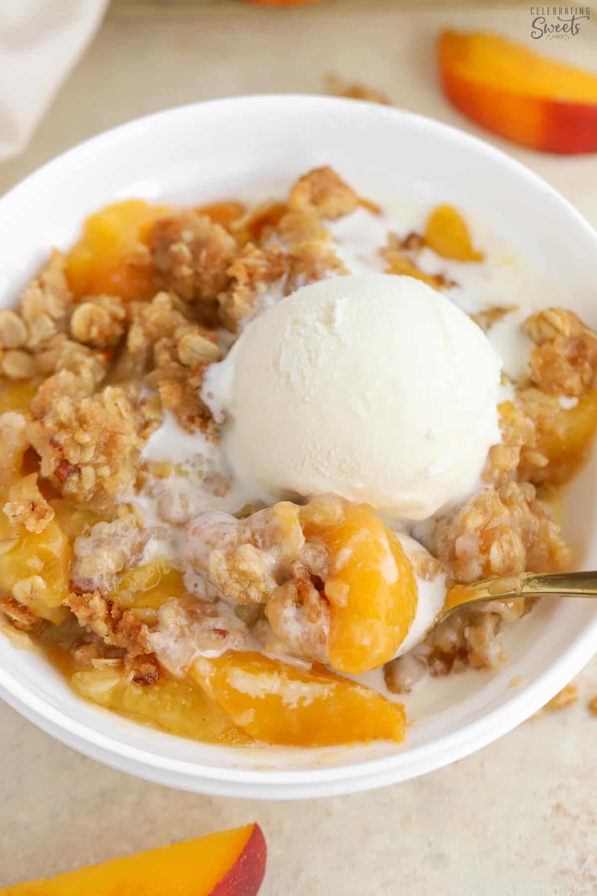 Peach crisp topped with vanilla ice cream in a white bowl.
