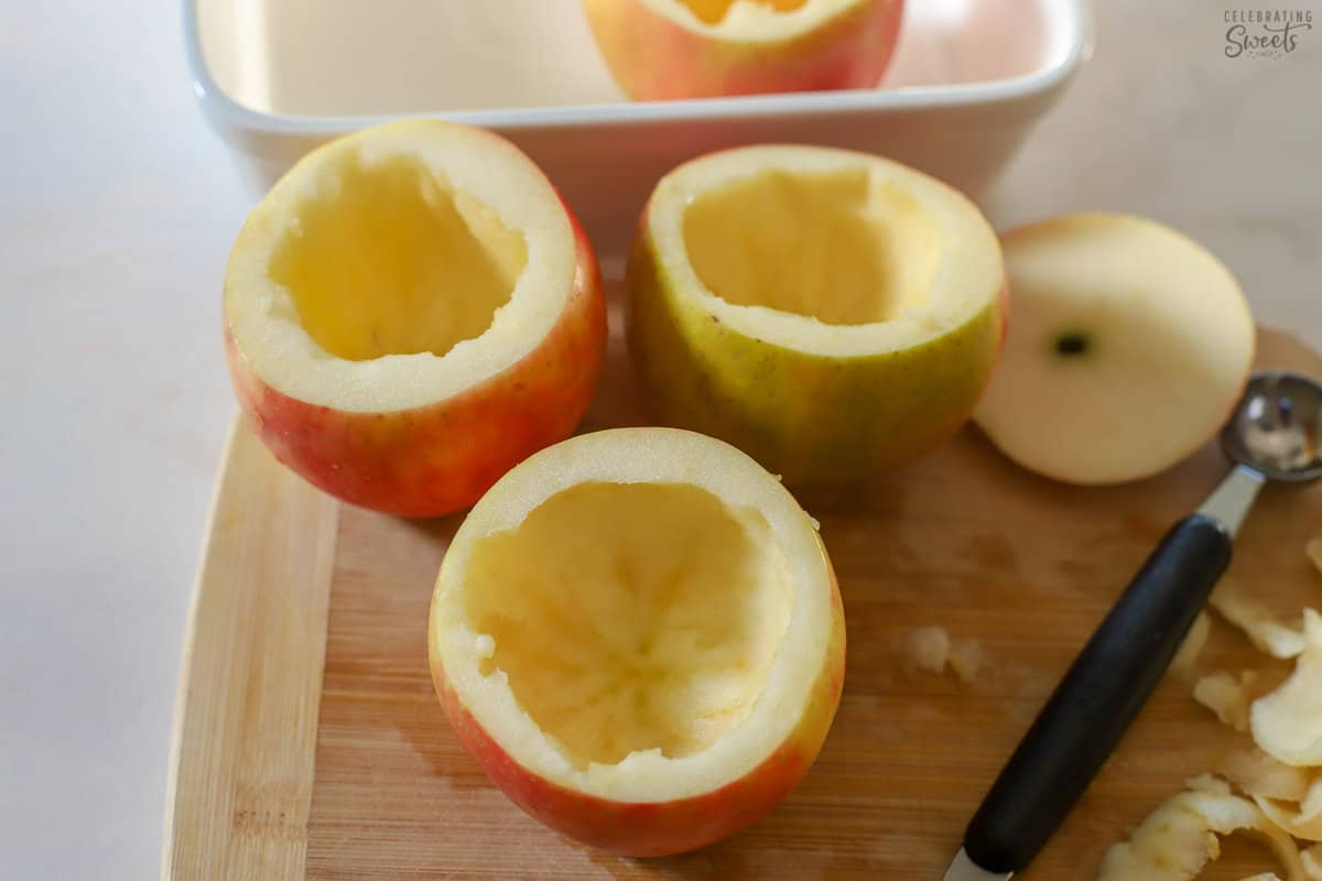 Apples with the middle scooped out sitting on a wood cutting board.