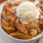 Apple cobbler in a white bowl topped with vanilla ice cream.