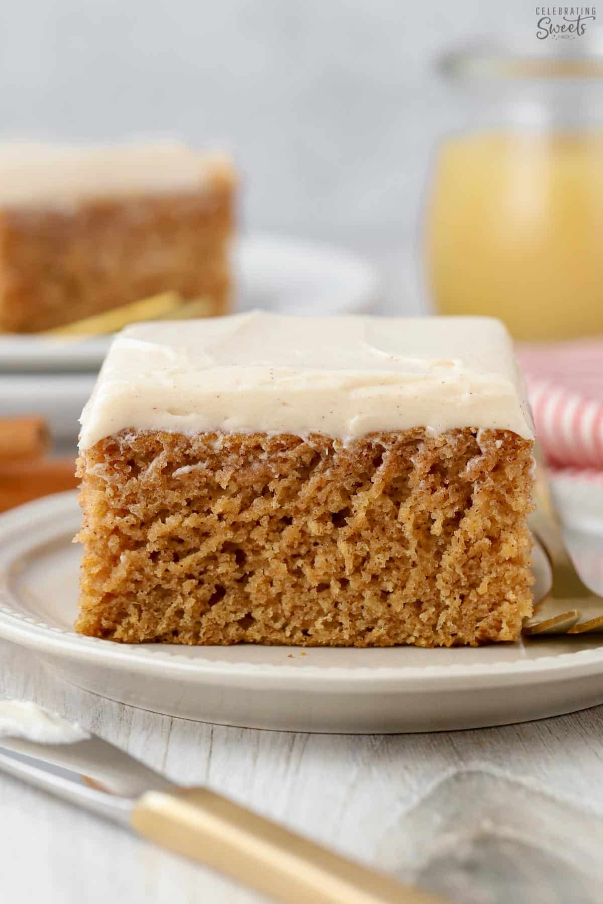Slice of applesauce cake topped with cream cheese frosting on a white plate with a gold fork.