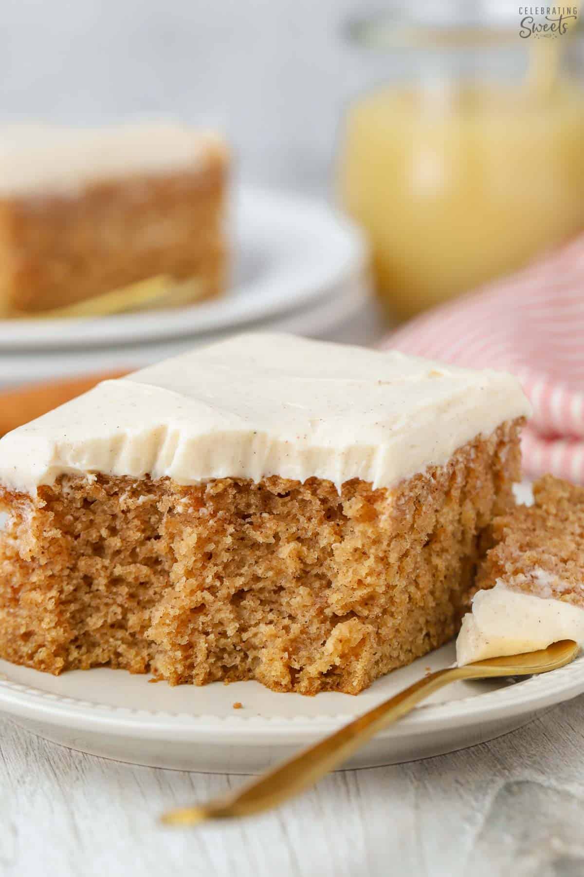 Slice of applesauce cake topped with cream cheese frosting on a small plate with a gold fork.
