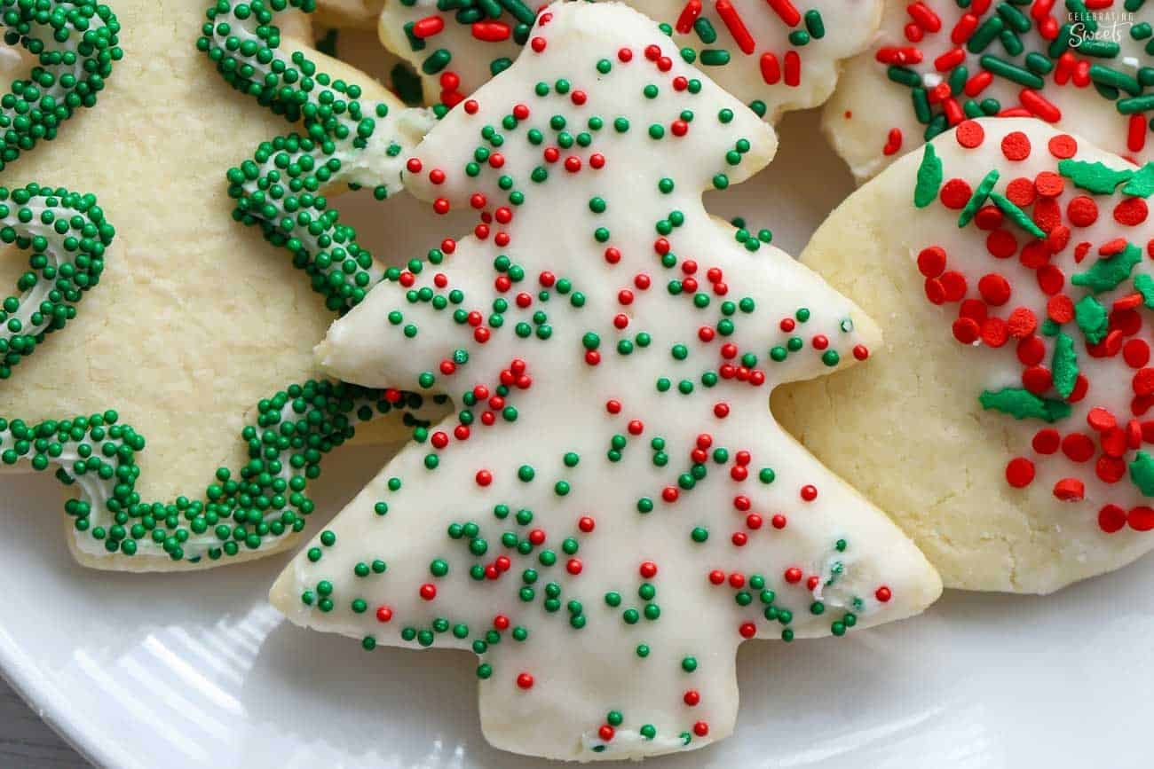 White frosted Christmas tree cutout cookie topped with red and green sprinkles.