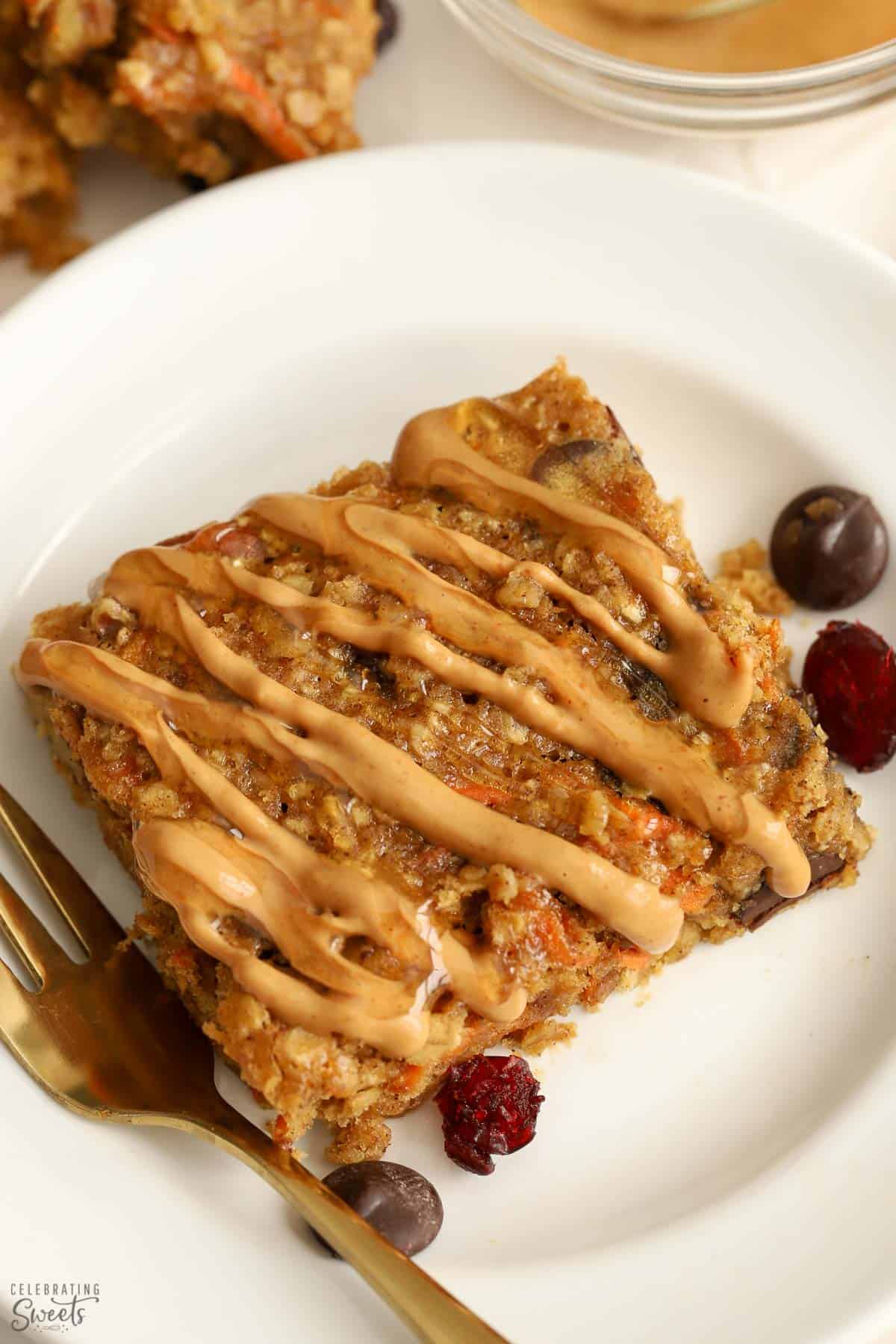 Breakfast bar drizzled with peanut butter on a white plate with a gold fork.