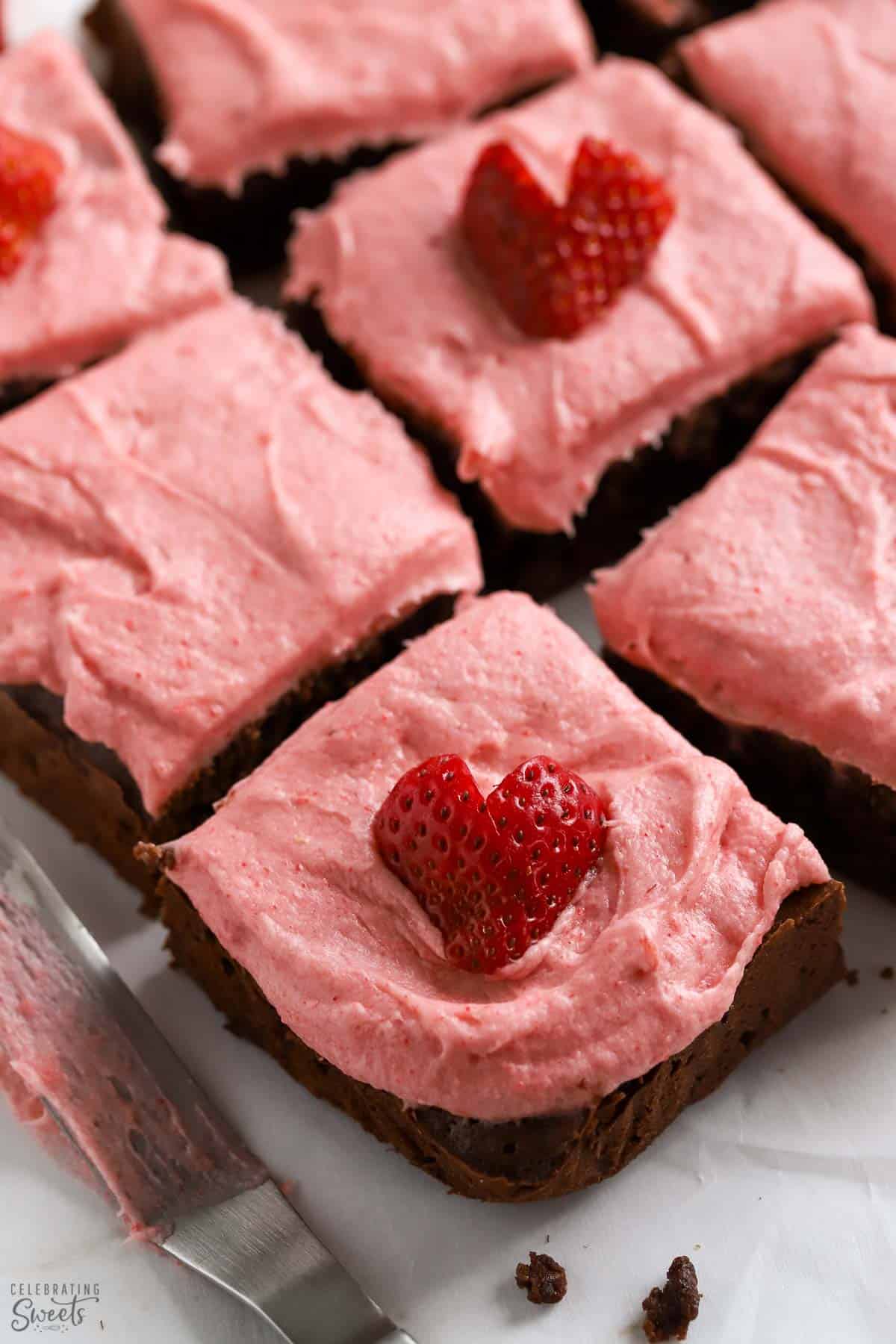 Strawberry brownies on parchment paper topped with heart shaped strawberries.