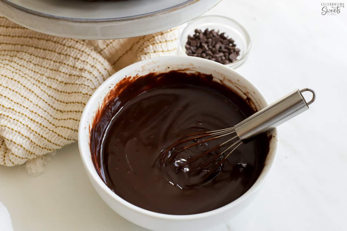 Chocolate ganache in a white bowl with a whisk.