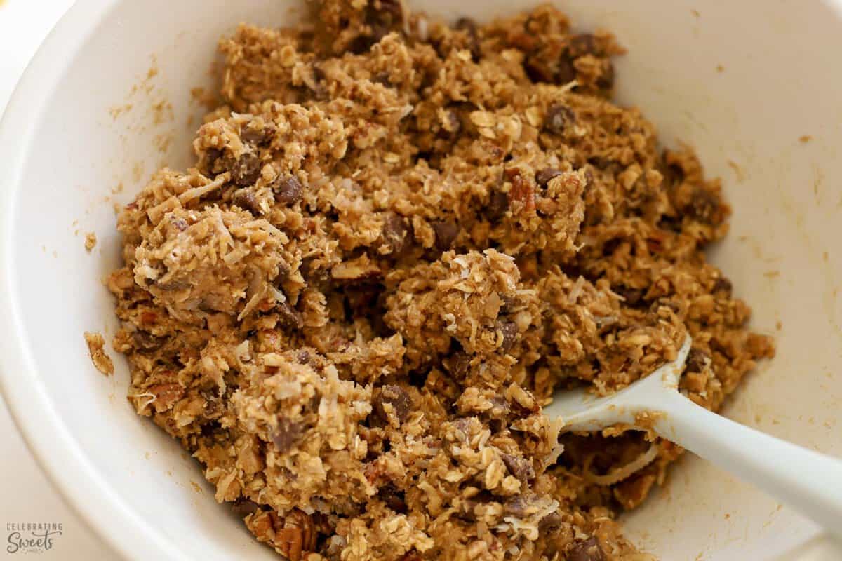Cowboy cookie dough in a white bowl with a grey spatula.