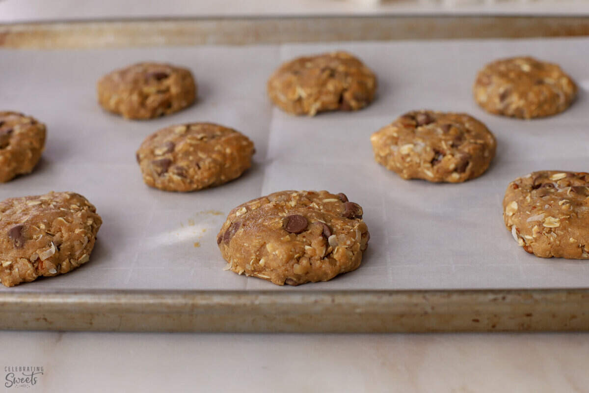 Discs of unbaked cowboy cookie dough on a parchment lined baking sheet.