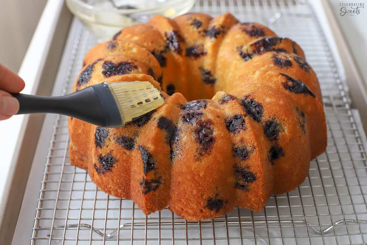 Lemon syrup being brushed on a lemon blueberry bundt cake.