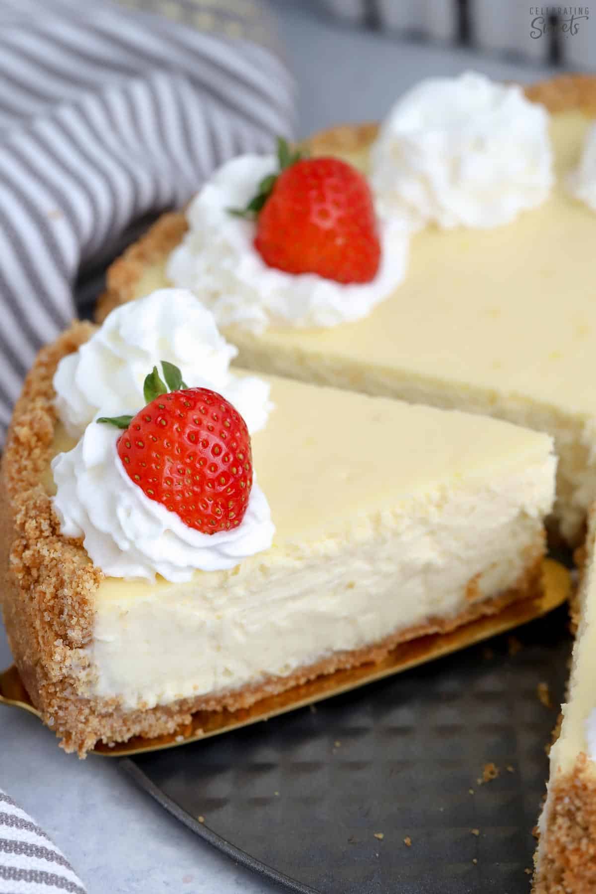 A slice of Greek yogurt cheesecake topped with a strawberry on a gold spatula.