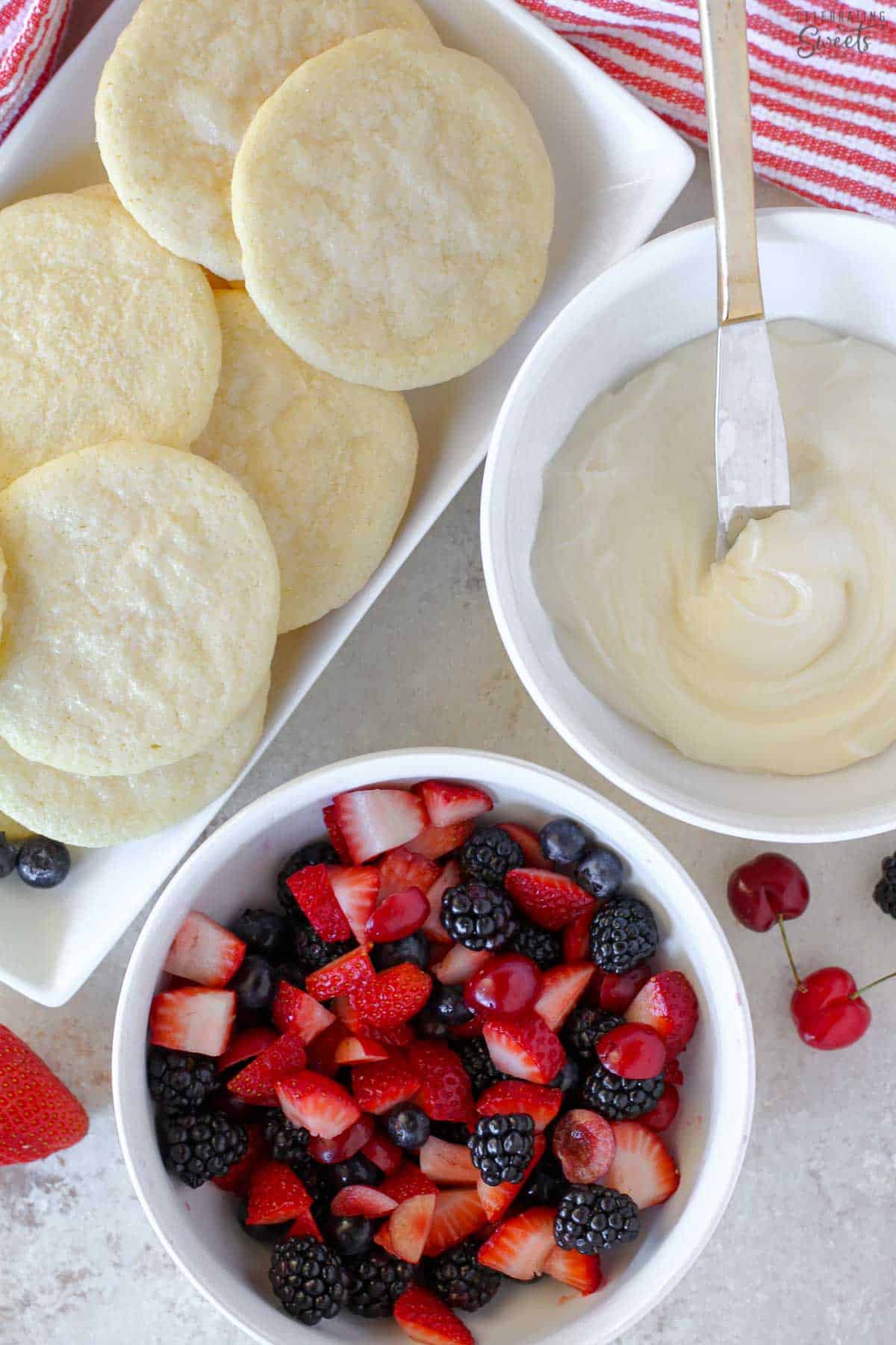 Ingredients for sugar cookie fruit tarts: sugar cookies, a bowl of frosting, and a bowl of berries.