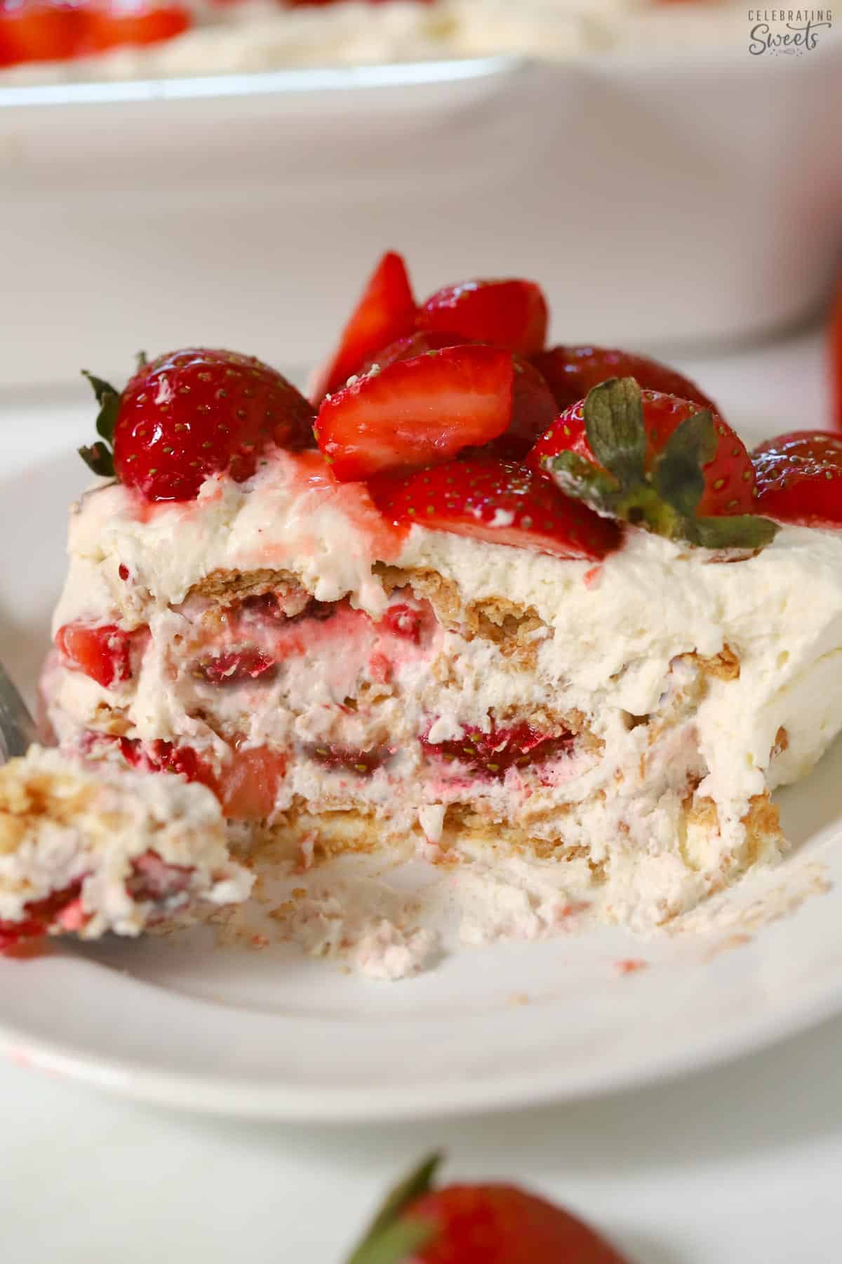Slice of a strawberry icebox cake topped with fresh strawberries on a white plate.