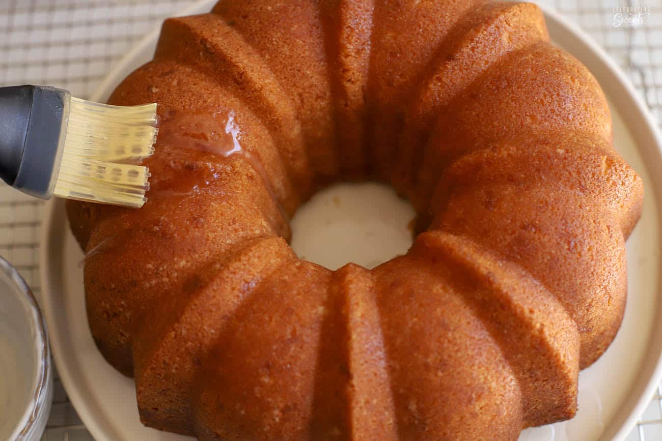 Bundt cake on a beige plated being brushed with syrup.