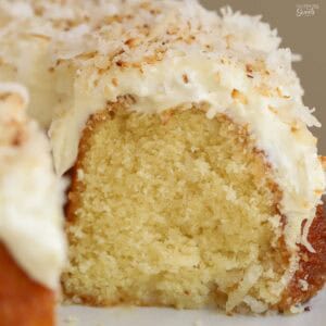 Closeup of coconut bundt cake topped with frosting and shredded coconut on a grey plate.