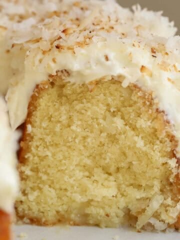 Closeup of coconut bundt cake topped with frosting and shredded coconut on a grey plate.