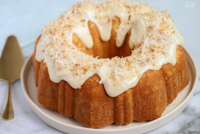 Coconut bundt cake topped with frosting and toasted coconut on a beige plate.