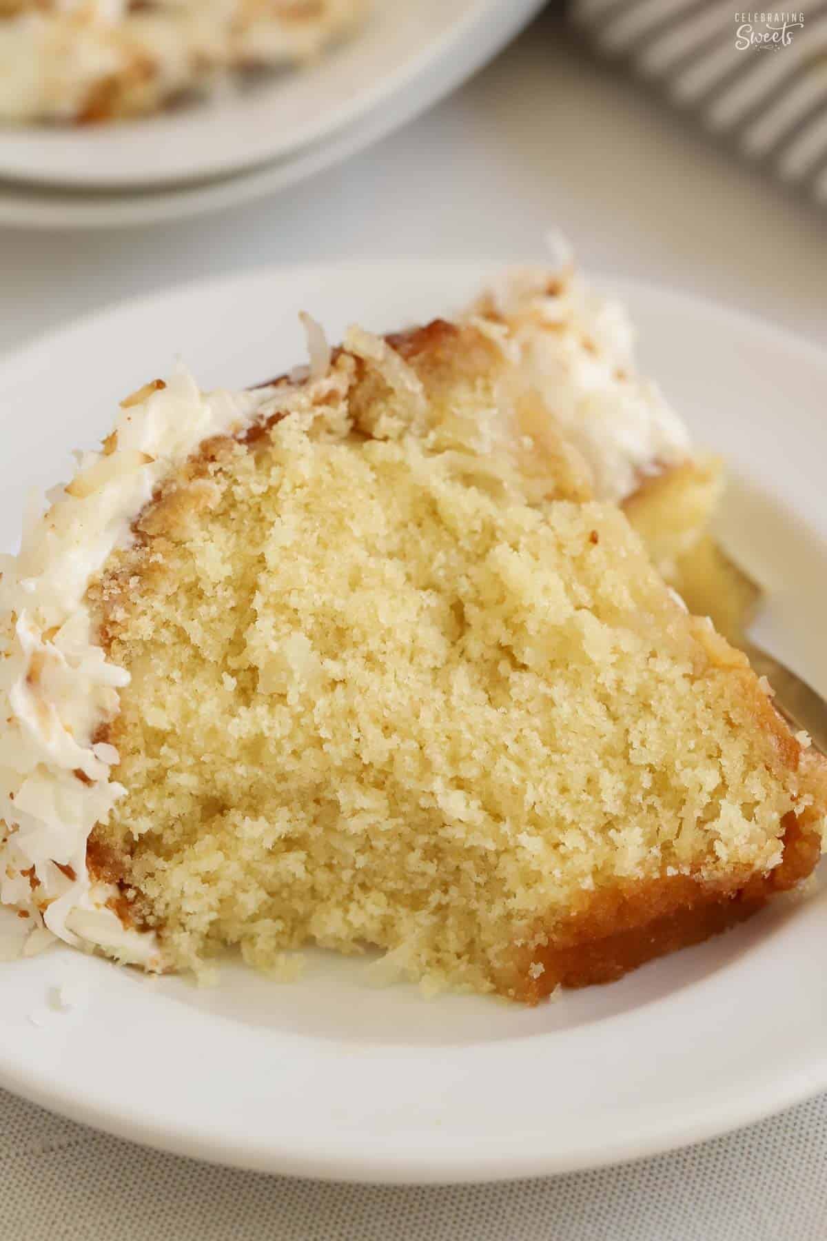Slice of coconut cake on a white plate with a gold fork in the background,
