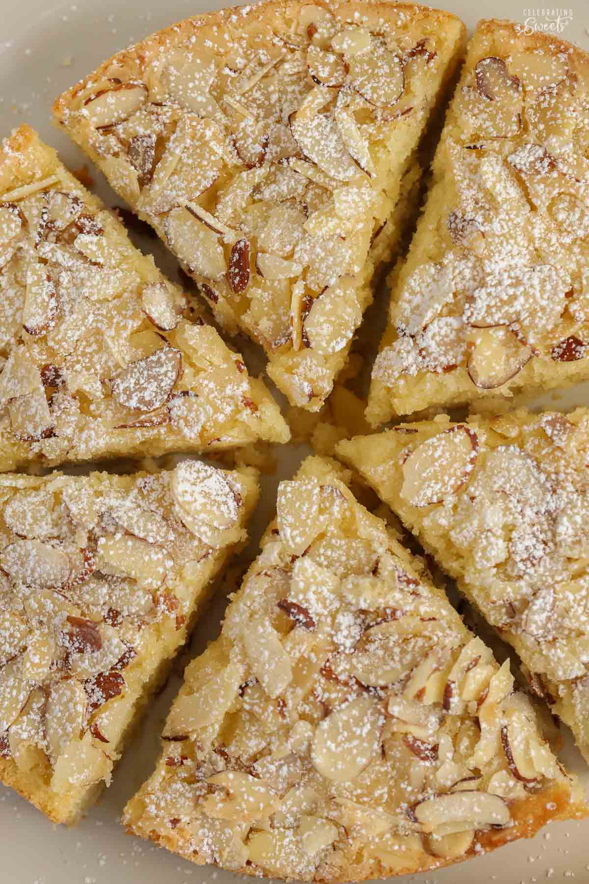 Overhead view of 6 slices of almond cake topped with sliced almonds on a grey plate,